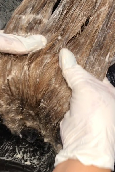 Hairstylist's gloved hands applying formula to hair.