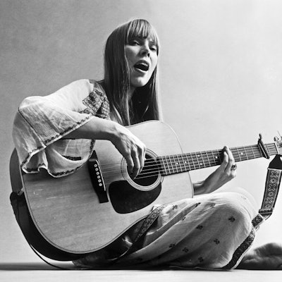 Joni Mitchell wears long, straight hairstyle paired with brow skimming bangs.