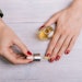 A person with red nail polish applies cuticle oil to their fingernails.