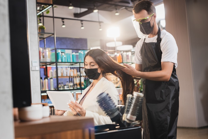 Hairdresser in face shield and mask, with a client.