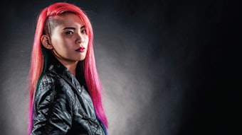 Person with vivid pink hair stands against a black backdrop.