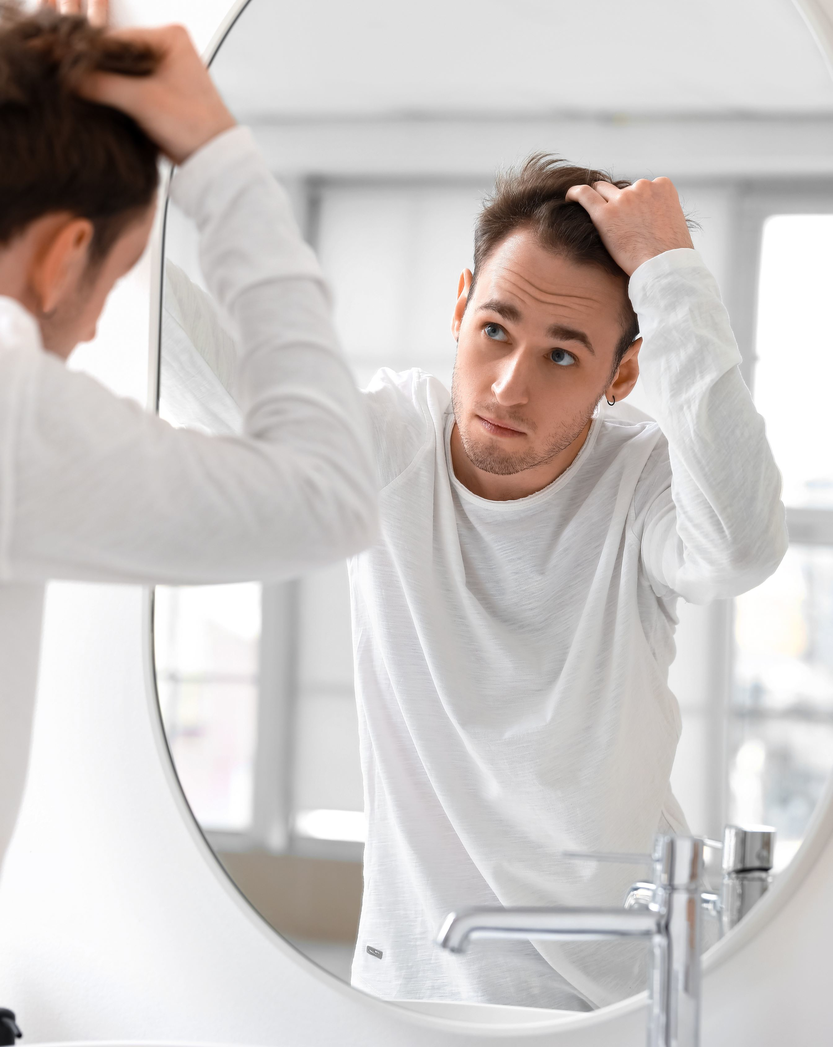 Young man with hair loss problem looking in mirror at home