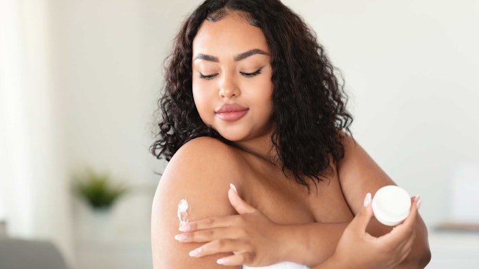 woman in bathroom applying soothing skin cream to her shoulder relaxed facial expression