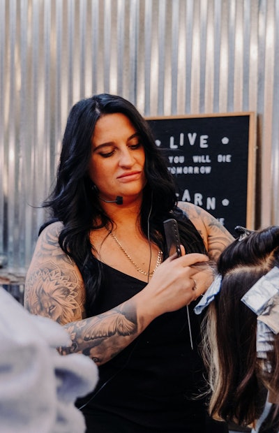 Gina Sicard applying foils to a model while educating on stage.