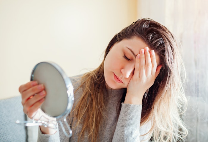 Stressed woman with dirty hair looking in mirror.