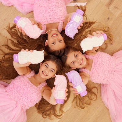 Girls in pink dresses hold products from Glimmer Wish's Unicorn line.