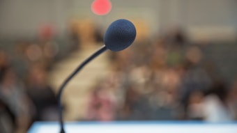 Point of View of view shot focused on a microphone on a podium with background blurred.
