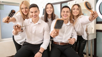 A group of hairstylists pose in a salon with hair tools in their hands.