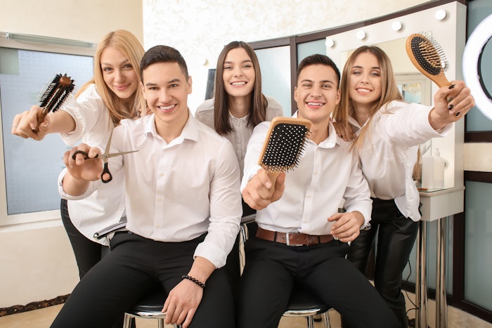 A group of hairstylists pose in a salon with hair tools in their hands.