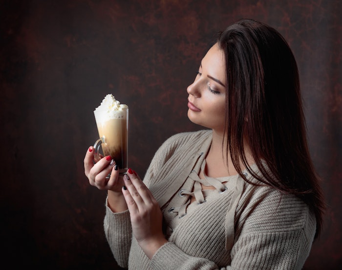 Woman with dark brunette hair holding a mocha coffee with whipped cream.