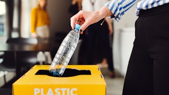 Close up of a person's hand recycling a plastic water bottle with the background blurred.