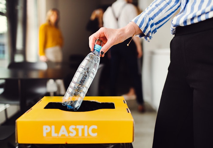 Close up of a person's hand recycling a plastic water bottle with the background blurred.