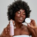Black woman curly hair holding lotion and cream products