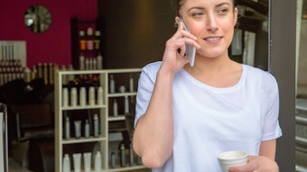 Hairstylist taking a break during her shift with a cup of coffee and talking on the phone.