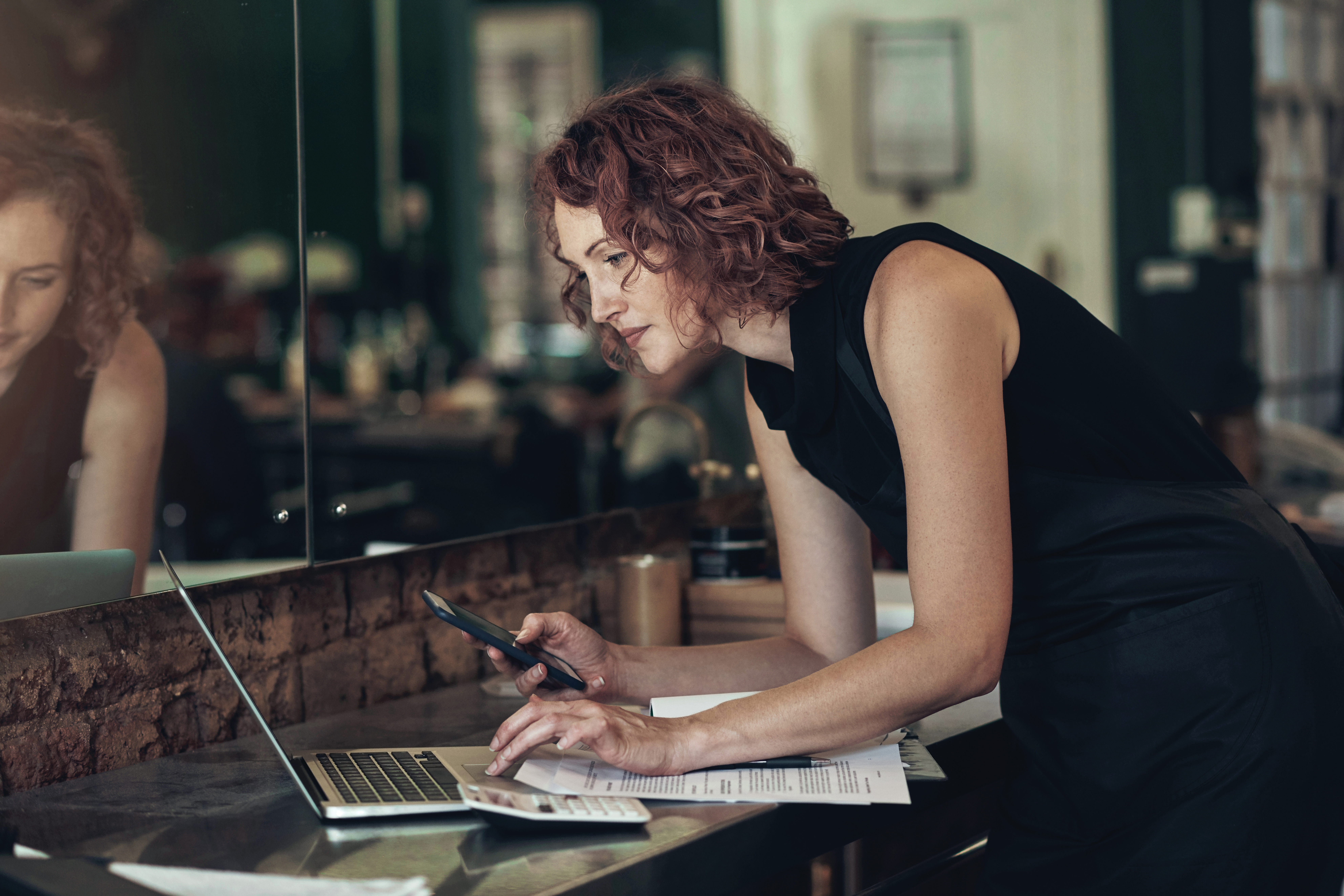 Stylist with phone in hand and working on laptop in a salon.