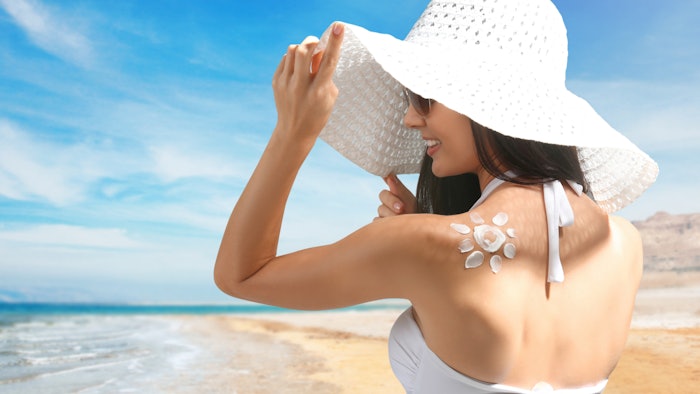 woman at beach in white hat wearing sunscreen sun drawing on shoulder.jpg