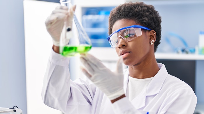 beautiful black female chemist examining liquid in flask