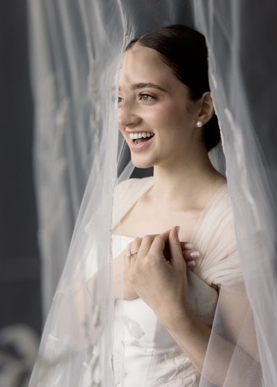 Nina's bridal client smiling in her finished updo and wearing her wedding dress.