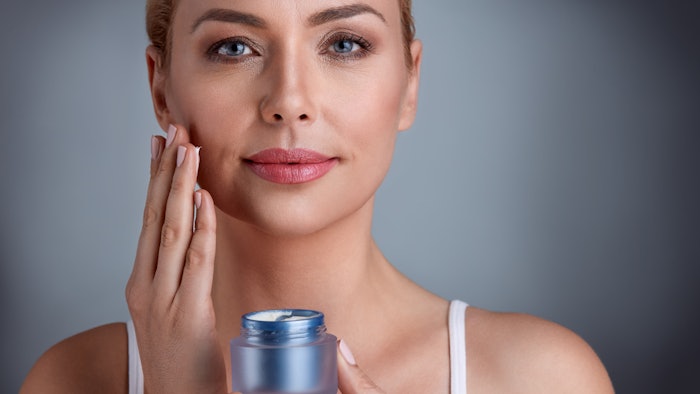 woman using skin cream smirking small jar of product