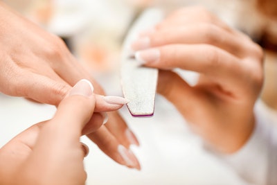 Nail tech files a client's nail using a nail file