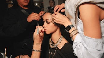 Behind the scenes at GUVANCH's NYFW show, where a model is being prepped by hairstylists and makeup artists.