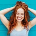 beautiful redhead teal background smiling holding hair up smiling