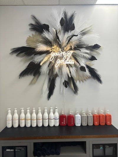 milk_shake and seven haircare products against a wall with a neon 'you're so golden' sign with feathers