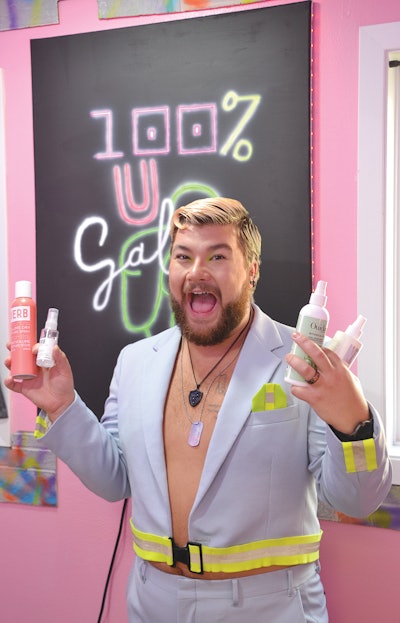 Willy Milard holding hair products in front of a 100% U Salon wall poster.