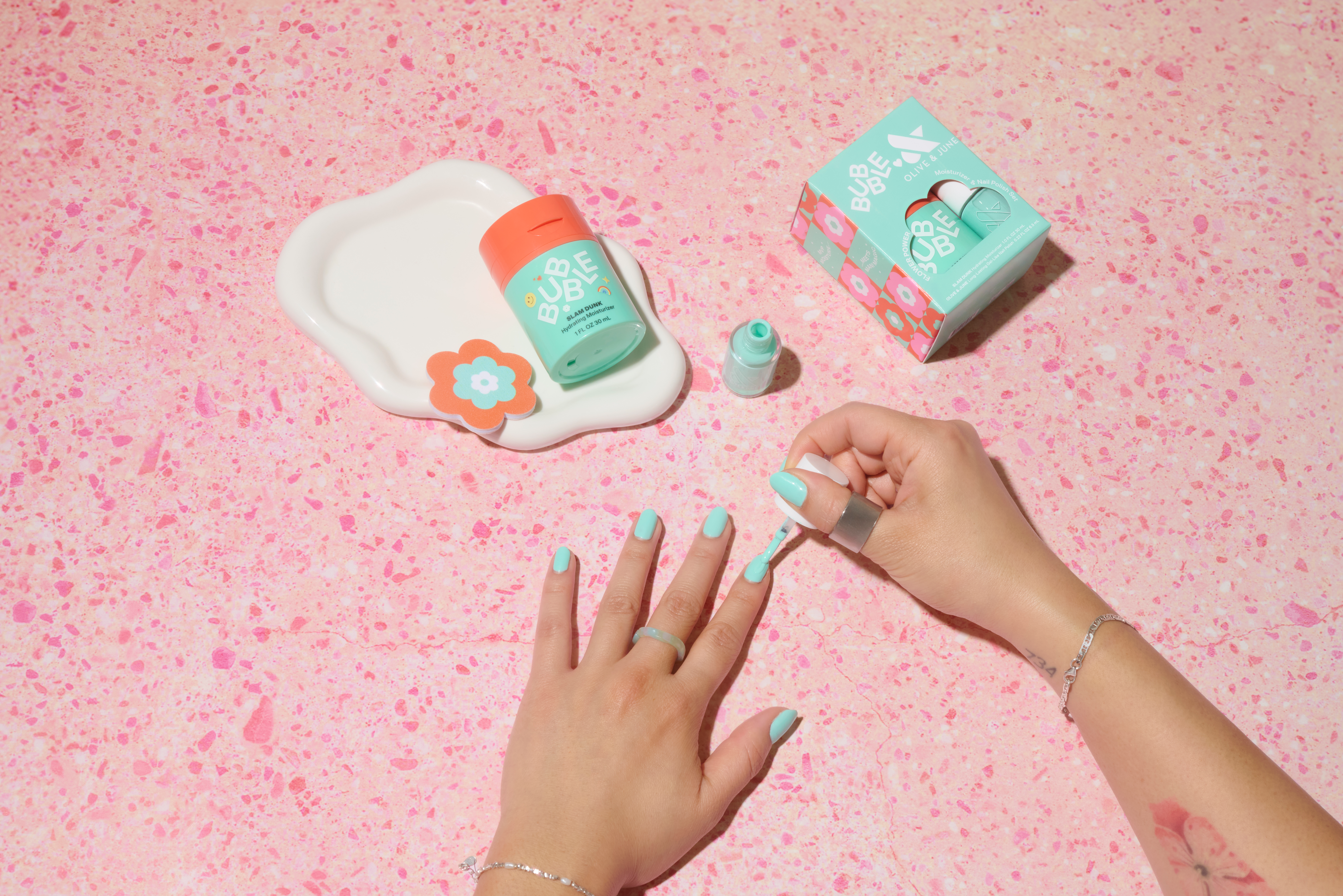 Bubble x Olive & June collection. A model paints her nails with a teal polish.