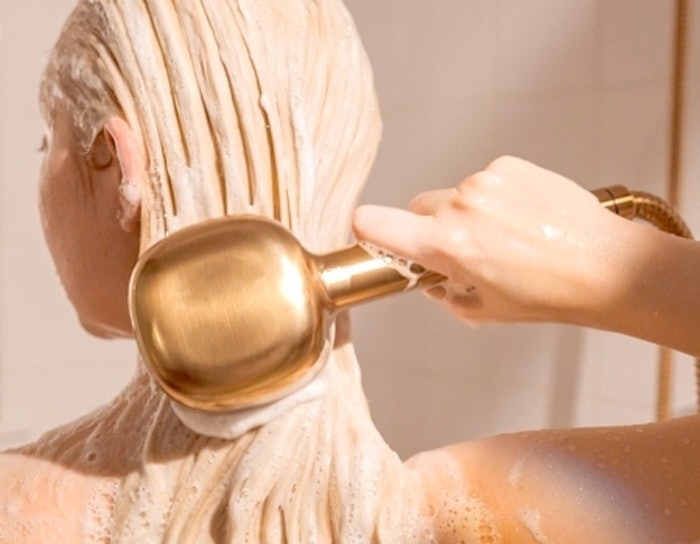 Woman with long blonde hair using gold canopy showerhead.