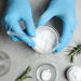 Hands in blue gloves preparing skincare or cosmetic ingredients in laboratory glassware