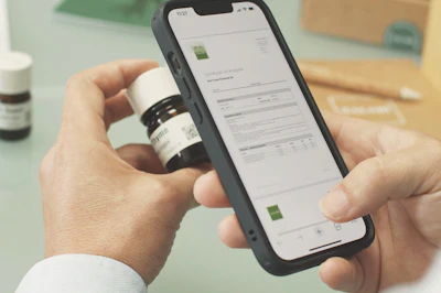 Person holding smartphone displaying product information next to a labeled bottle on a workspace