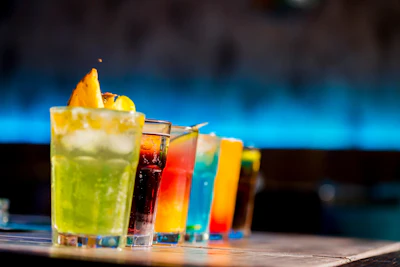 Colorful cocktails lined up on a bar counter with a blue-lit background