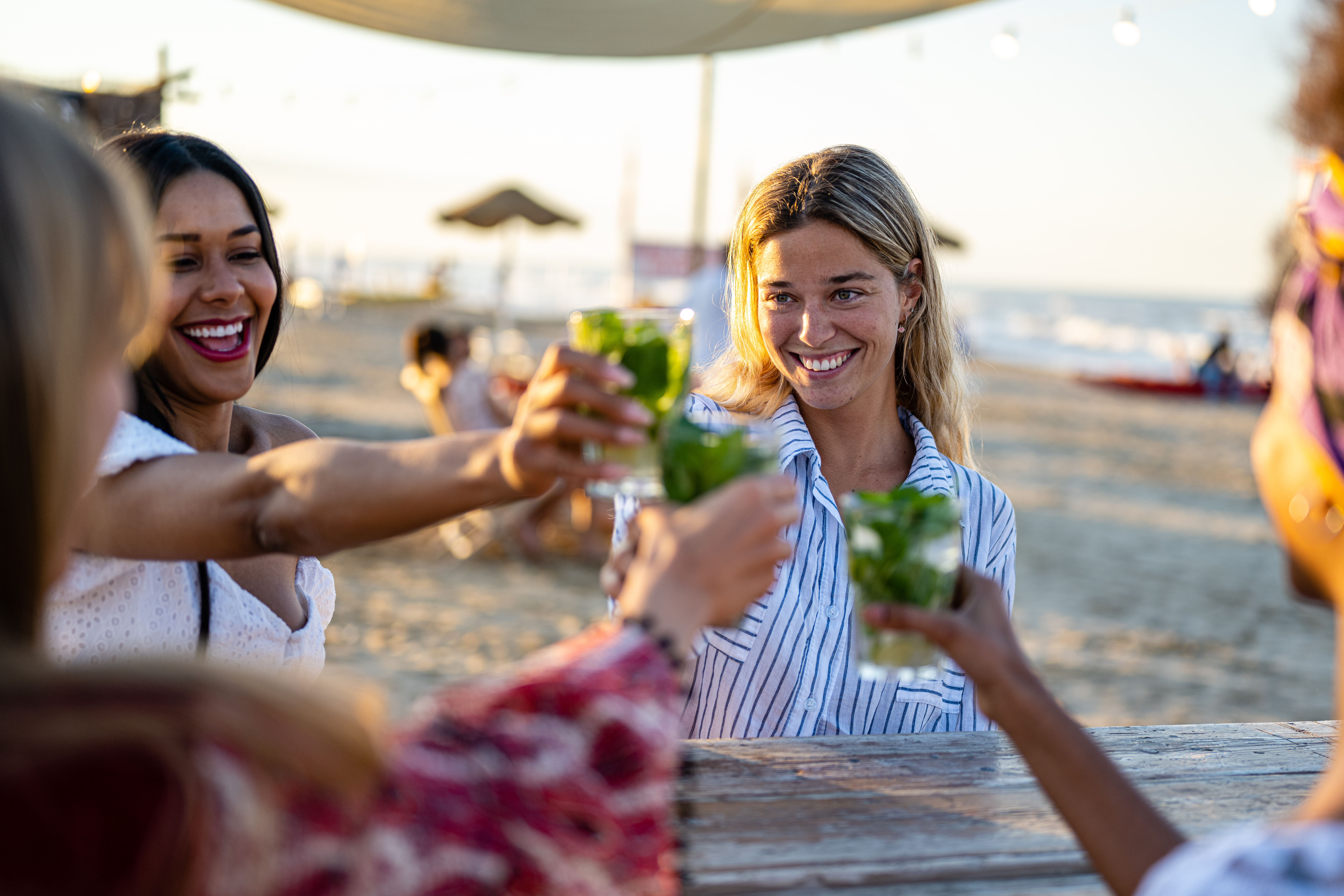 Friends toasting with drinks at a beach sunset celebration