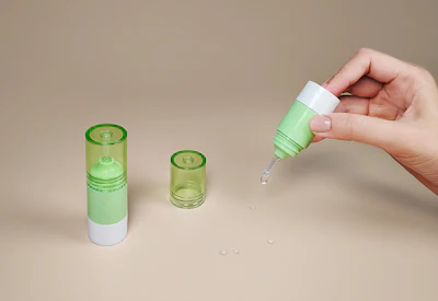 Hand dispensing green liquid serum from cosmetic bottle with matching product containers on neutral background