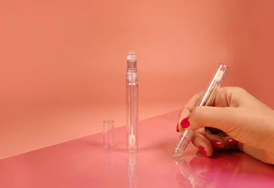 Hand holding clear glass perfume bottle with two additional bottles on coral background