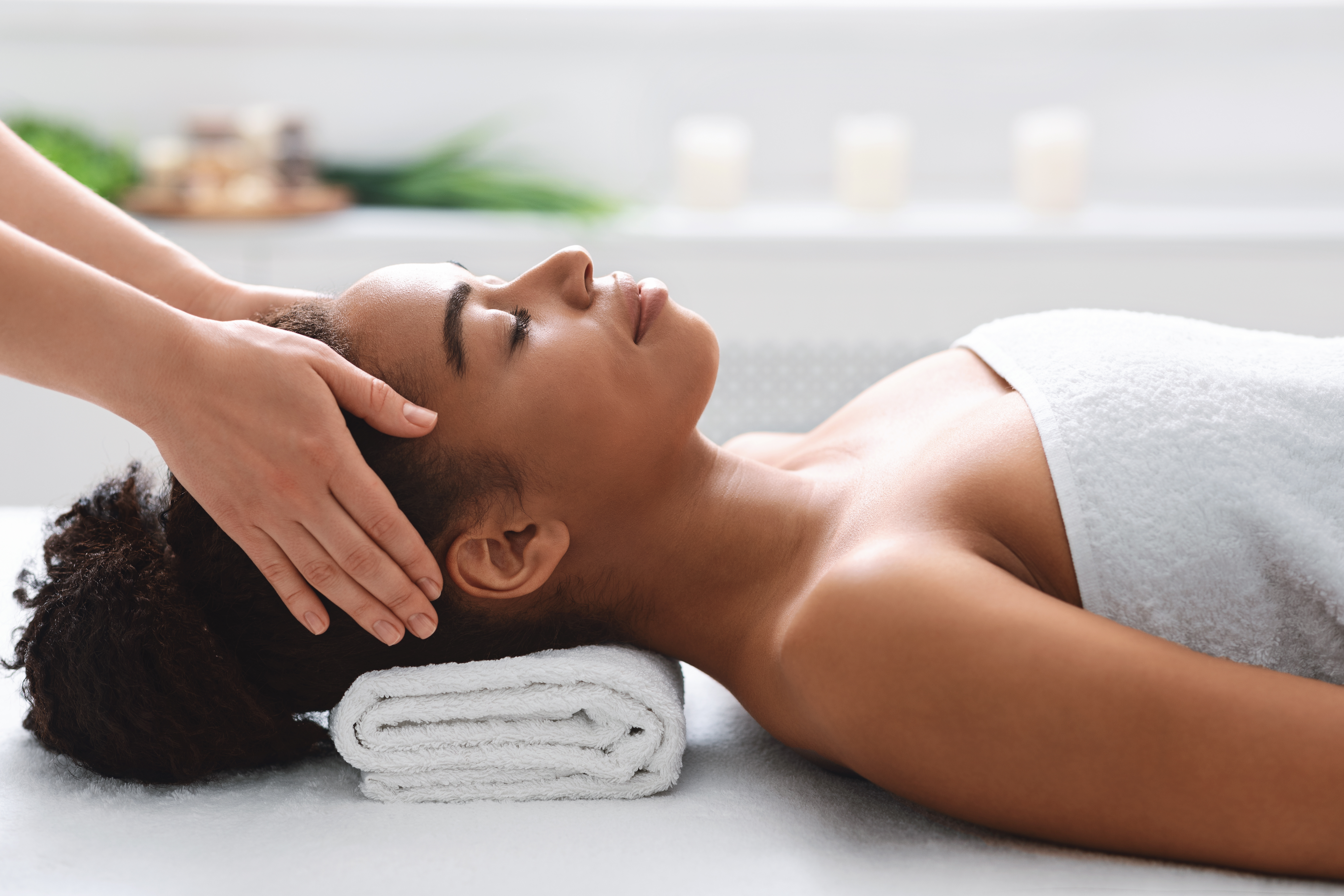 Woman receiving relaxing head massage at spa with white towel and candles in background