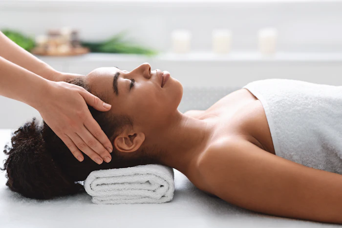 Woman receiving relaxing head massage at spa with white towel and candles in background