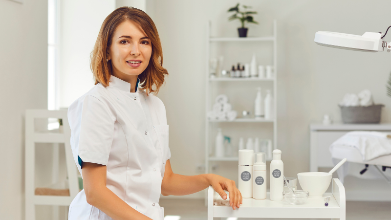 Professional woman in white coat presenting skincare products in modern spa treatment room