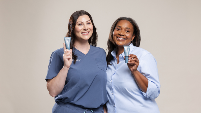 Two smiling women in professional attire posing together against a neutral beige background