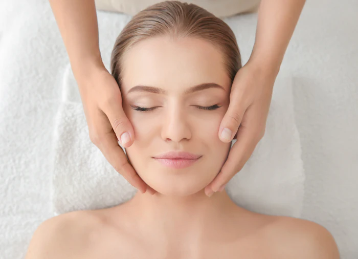 Woman receiving professional facial massage treatment at spa with eyes closed in relaxation