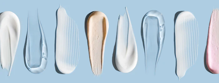 Array of cosmetic and skincare product swatches in white, cream, and pink tones on blue background