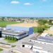 Aerial view of modern industrial facility with blue-roofed building, manufacturing structures, and surrounding agricultural fields