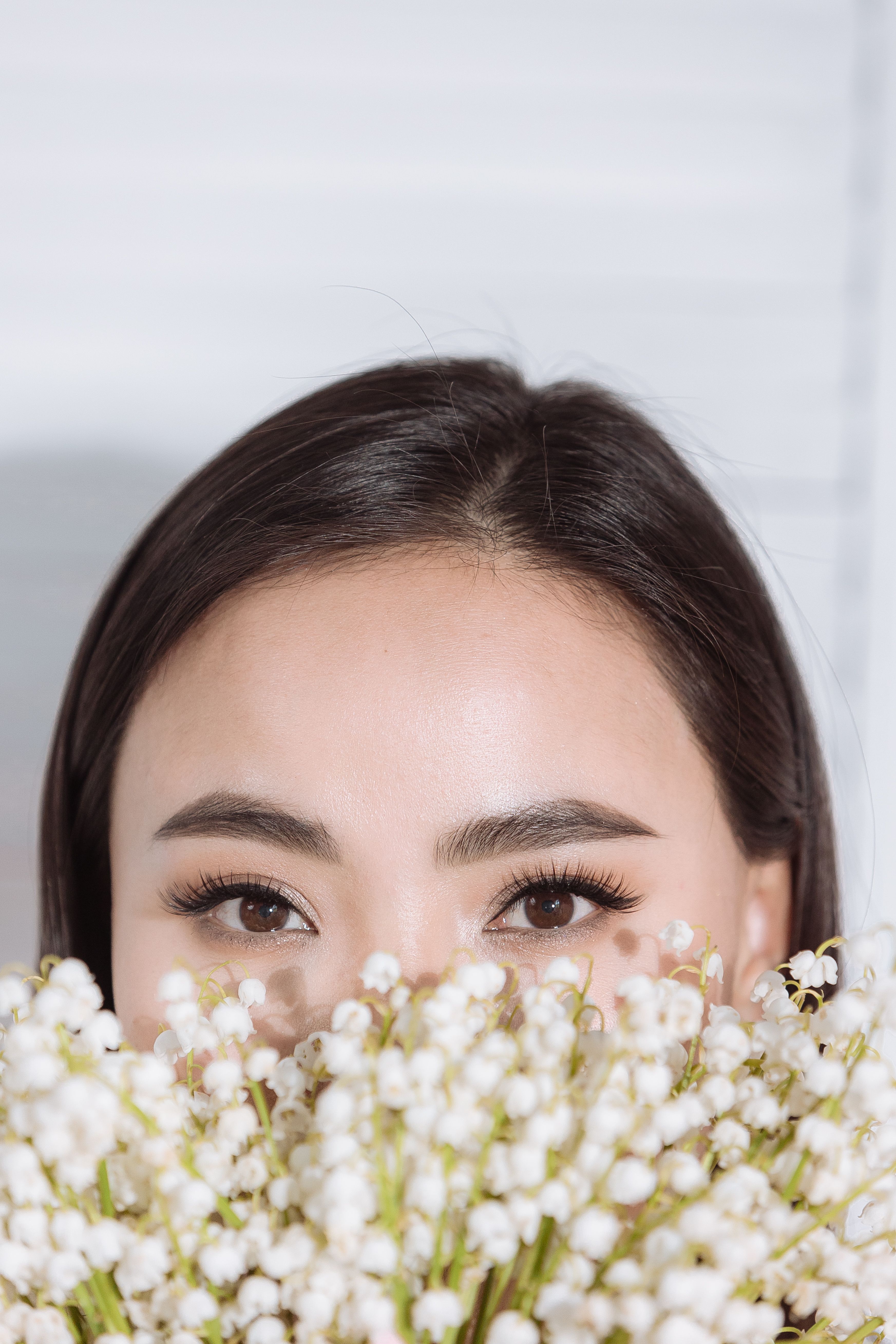 Woman's face partially hidden behind white baby's breath flowers with natural makeup and brown eyes