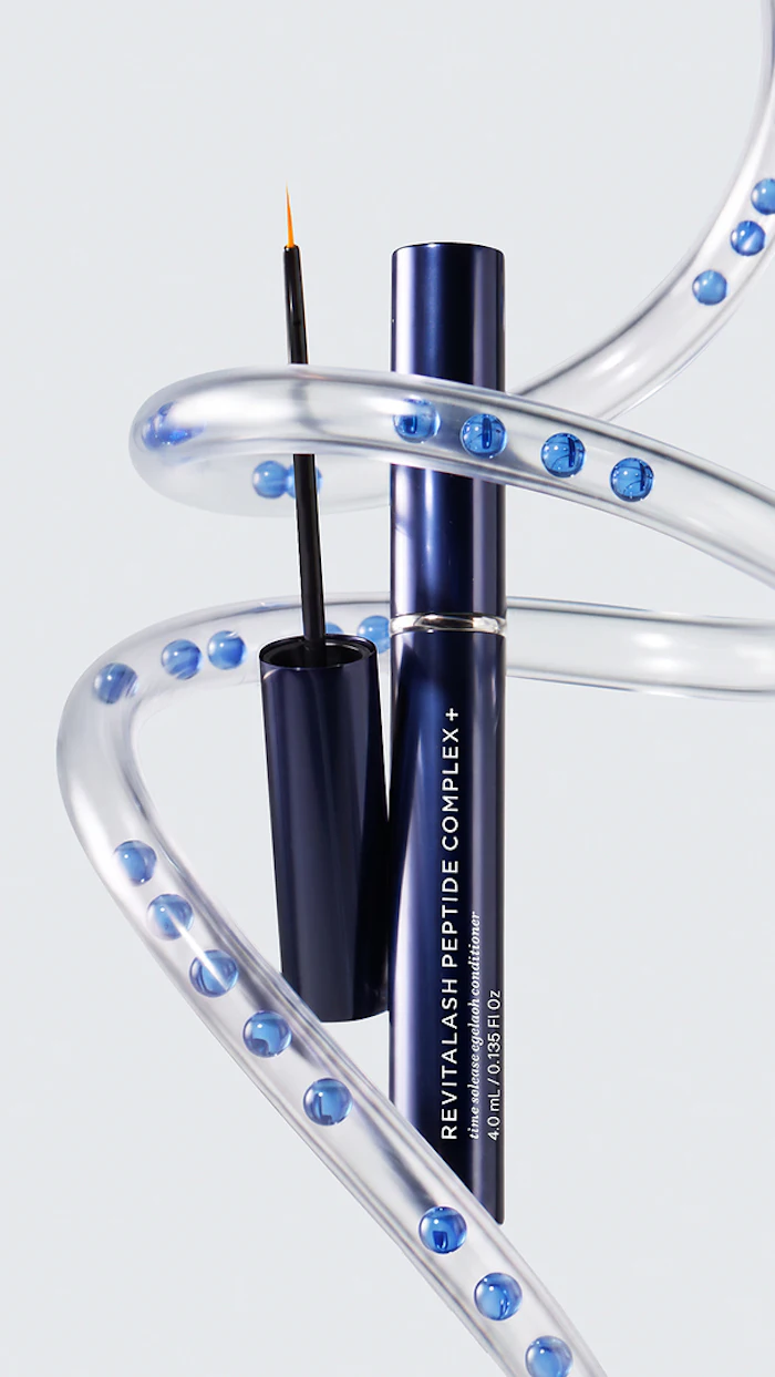 Revitalash Peptide Complex eyeliner with brush displayed among clear decorative tubes filled with blue spheres