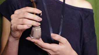 Woman holding a small jar of nail polish with neutral beige shade in both hands