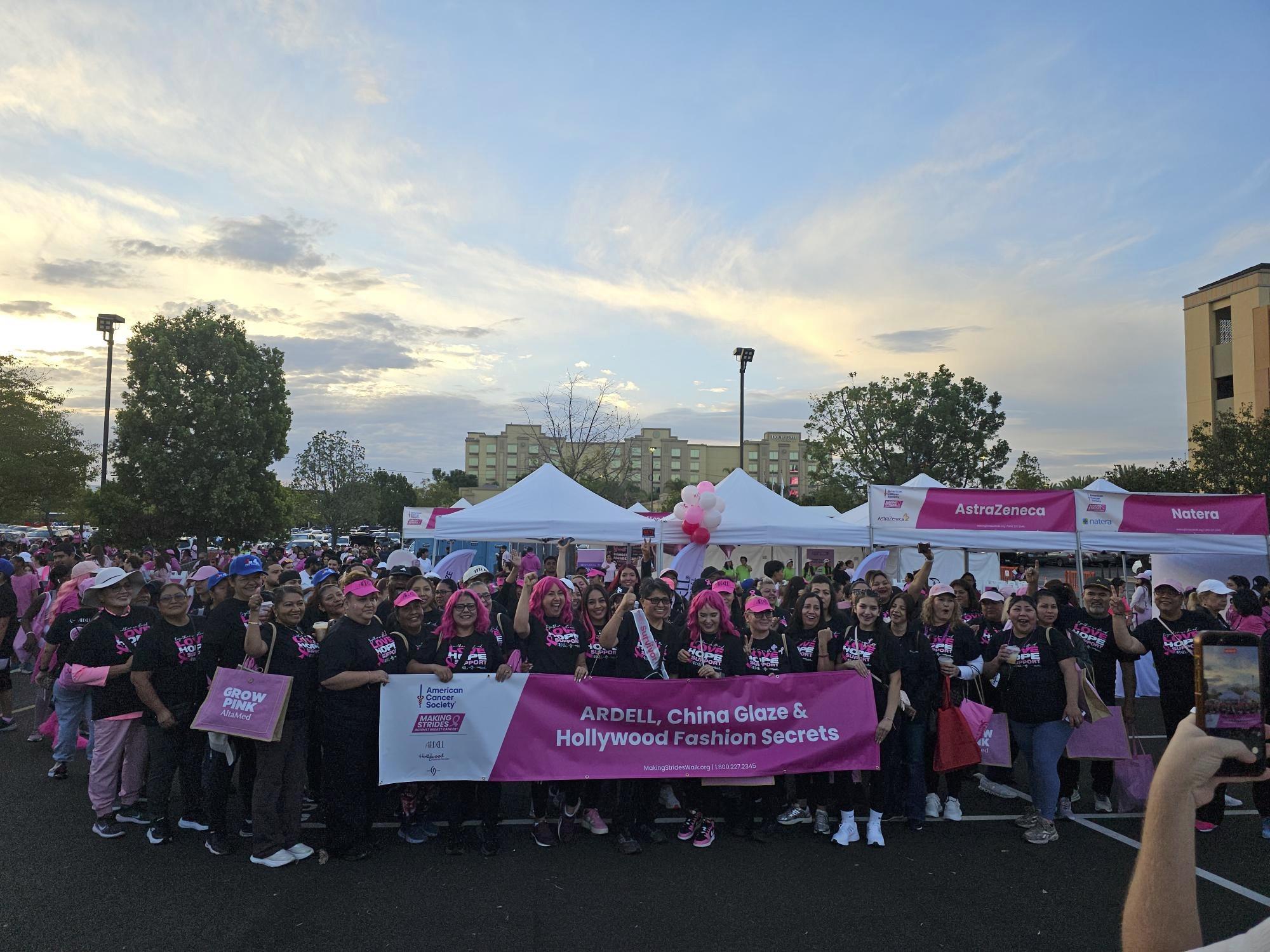 Large crowd wearing pink and black shirts at outdoor community event with branded tents and signage