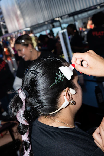 Person with dark braided hair adorned with white flower clips and pink ribbon at an indoor event or gathering