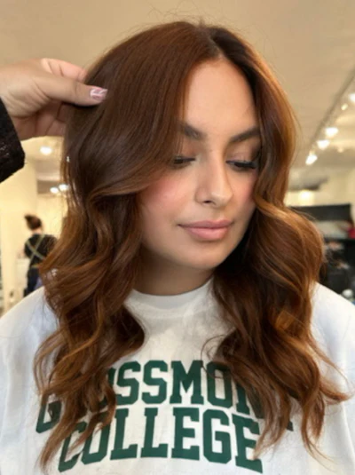 Woman with long wavy brown hair wearing white college t-shirt in indoor setting
