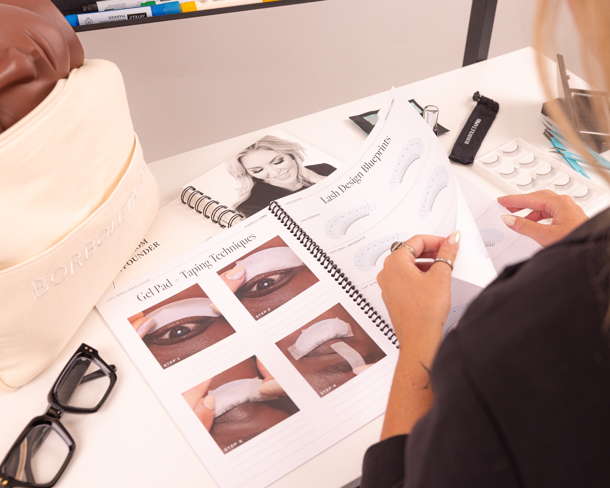 Beauty professional reviewing eye makeup application techniques with cosmetic products and instructional diagrams on workspace